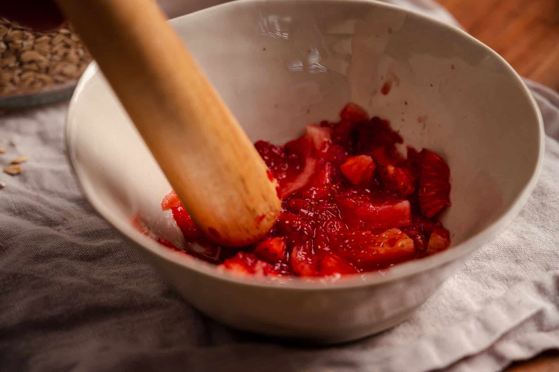Freshly muddles strawberries in a white bowl.