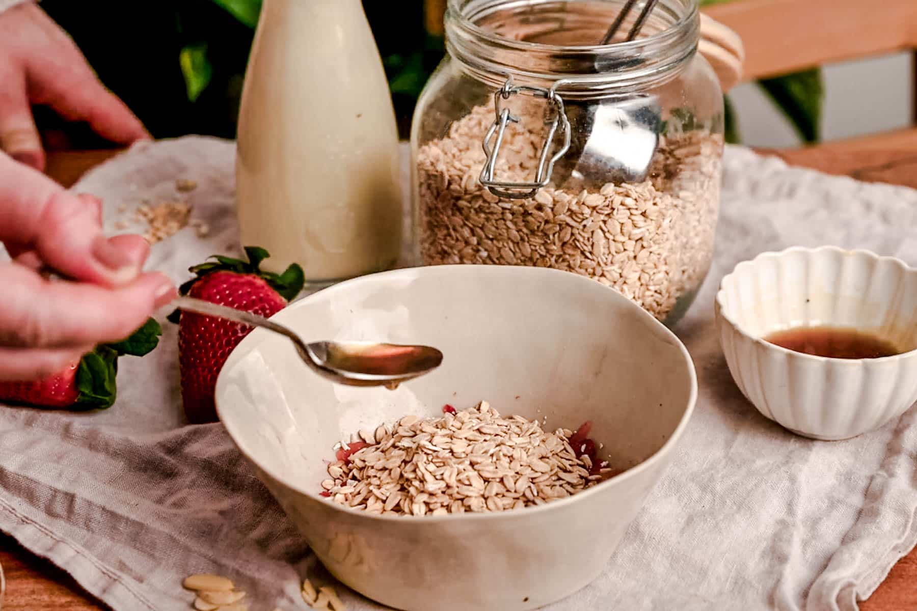 Drizzling maple syrup into a bowl with oats and strawberries.