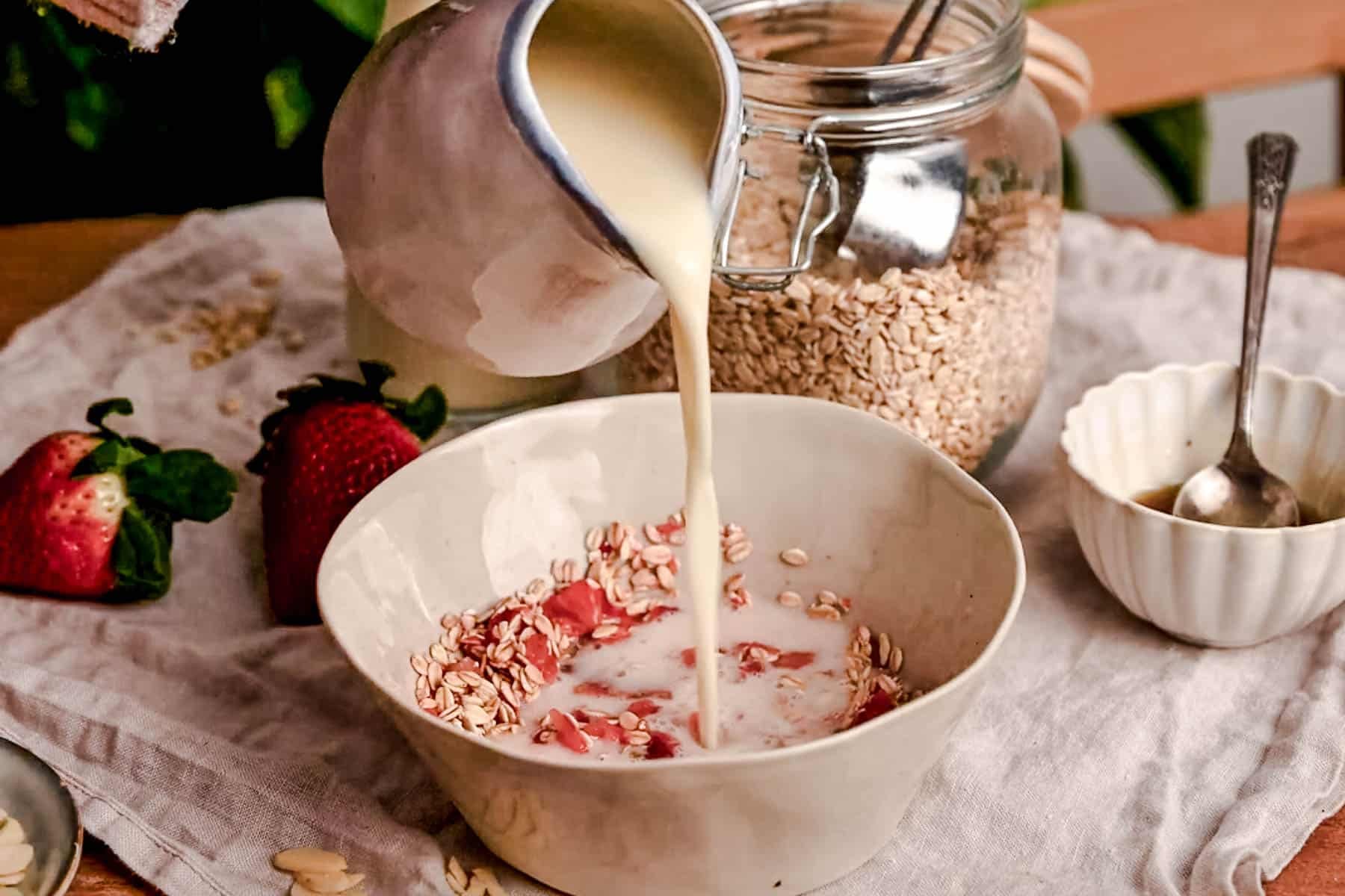 Pouring oat milk on top of the bowl of strawberry oats.
