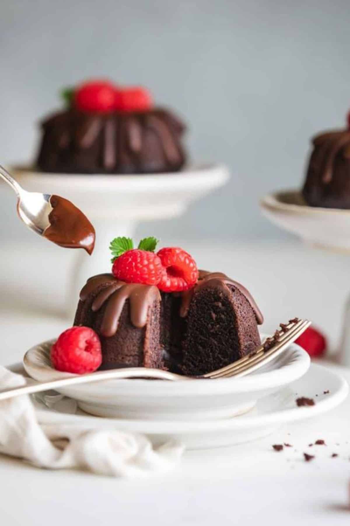 Three mini chocolate bundt cakes with drizzling chocolate and fresh raspberries.