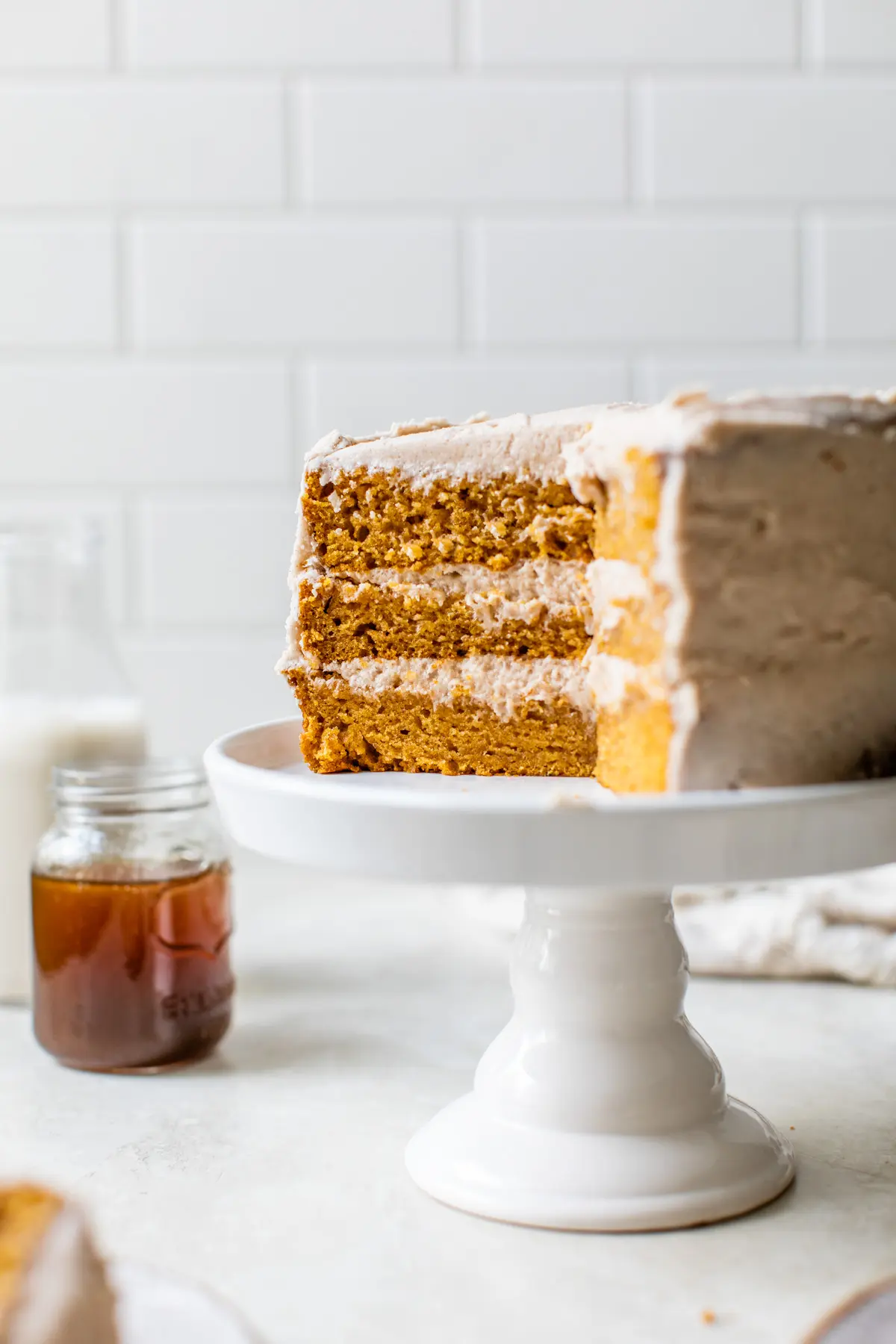 Three layer pumpkin cake with plenty of frosting on a white cake stand.