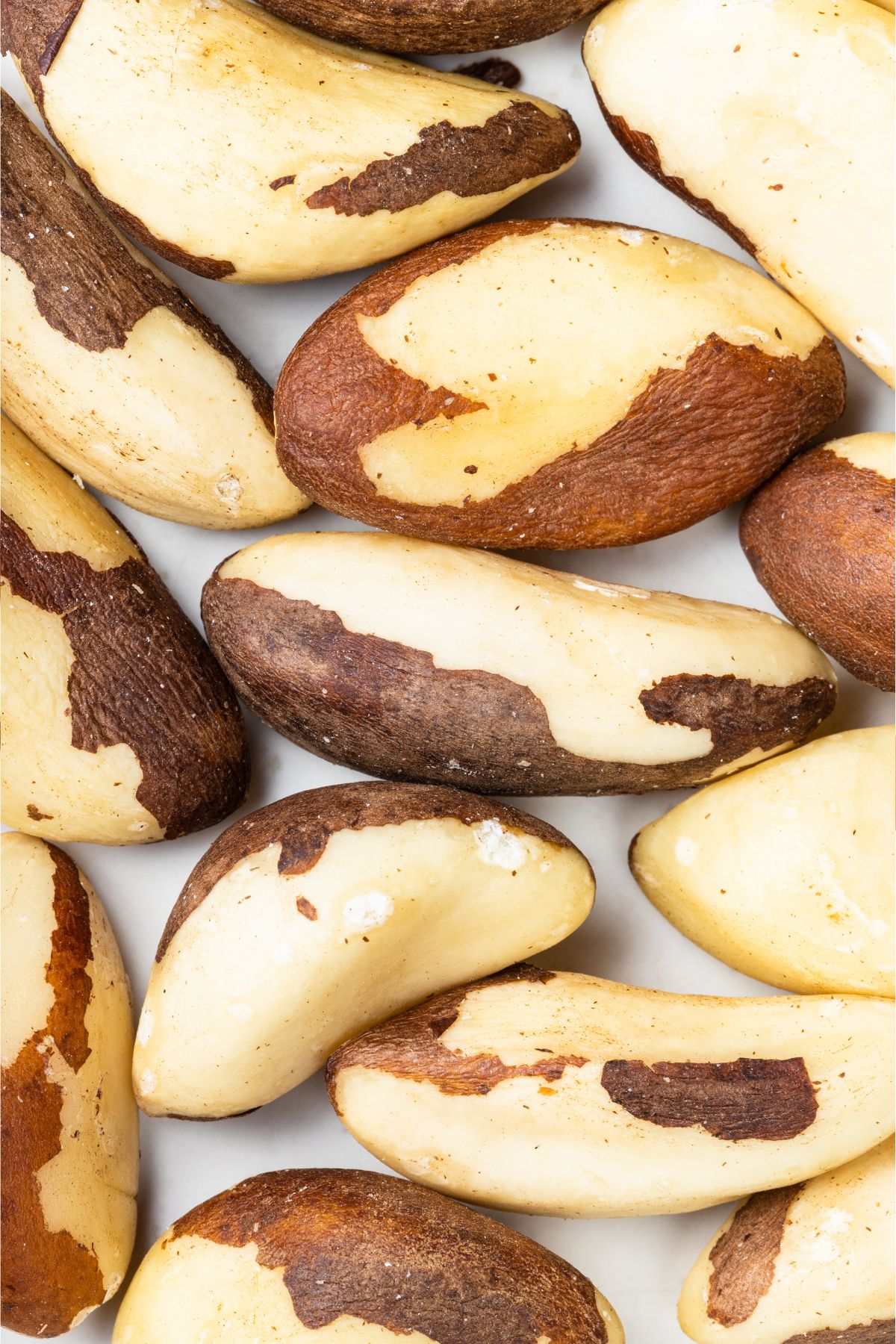 White counter covered in cream-white brazil nuts with some of their brown skin still on.