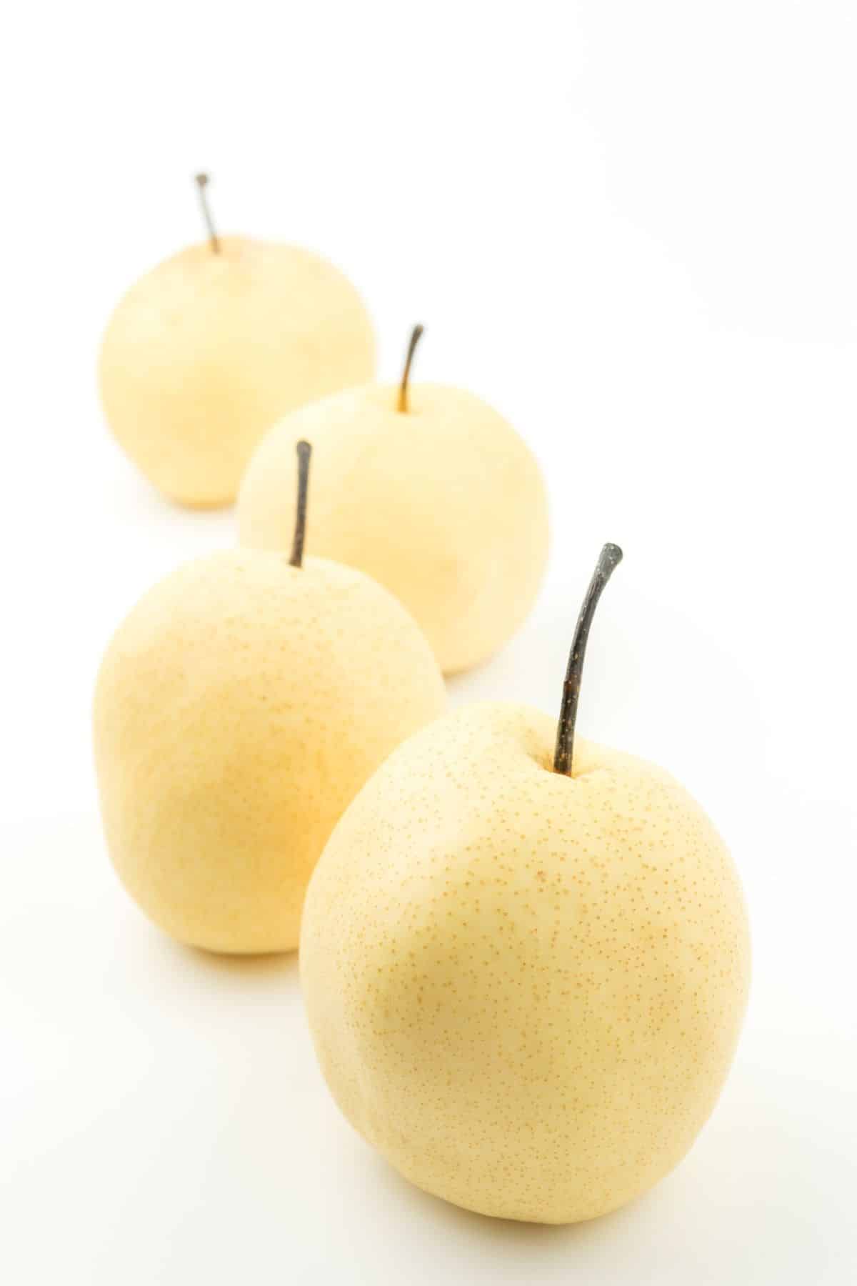 Four Chinese white pear with creamy skin on a white surface.