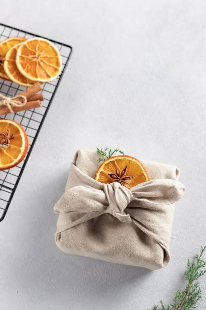 Christmas gift wrapped in linen fabric with dried oranges on top.