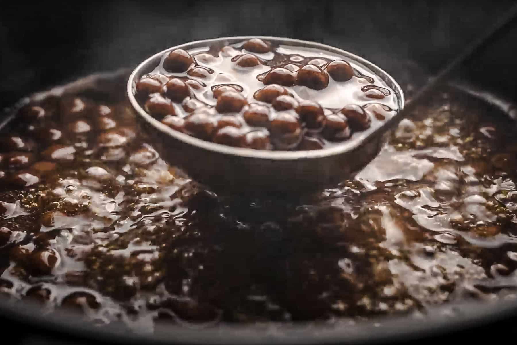 A ladle scoops cooked boba from a simmering pot.