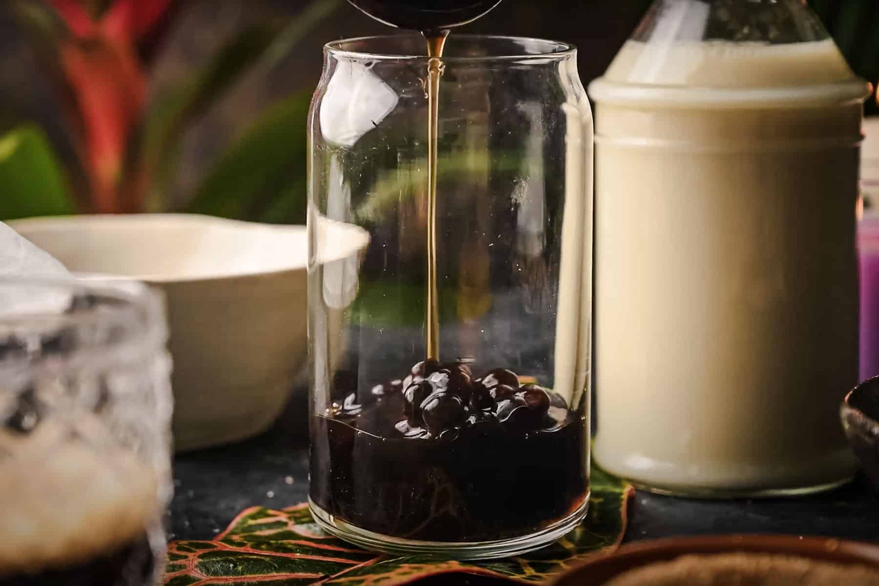 A glass with tapioca pearls is being filled with rich brown boba.