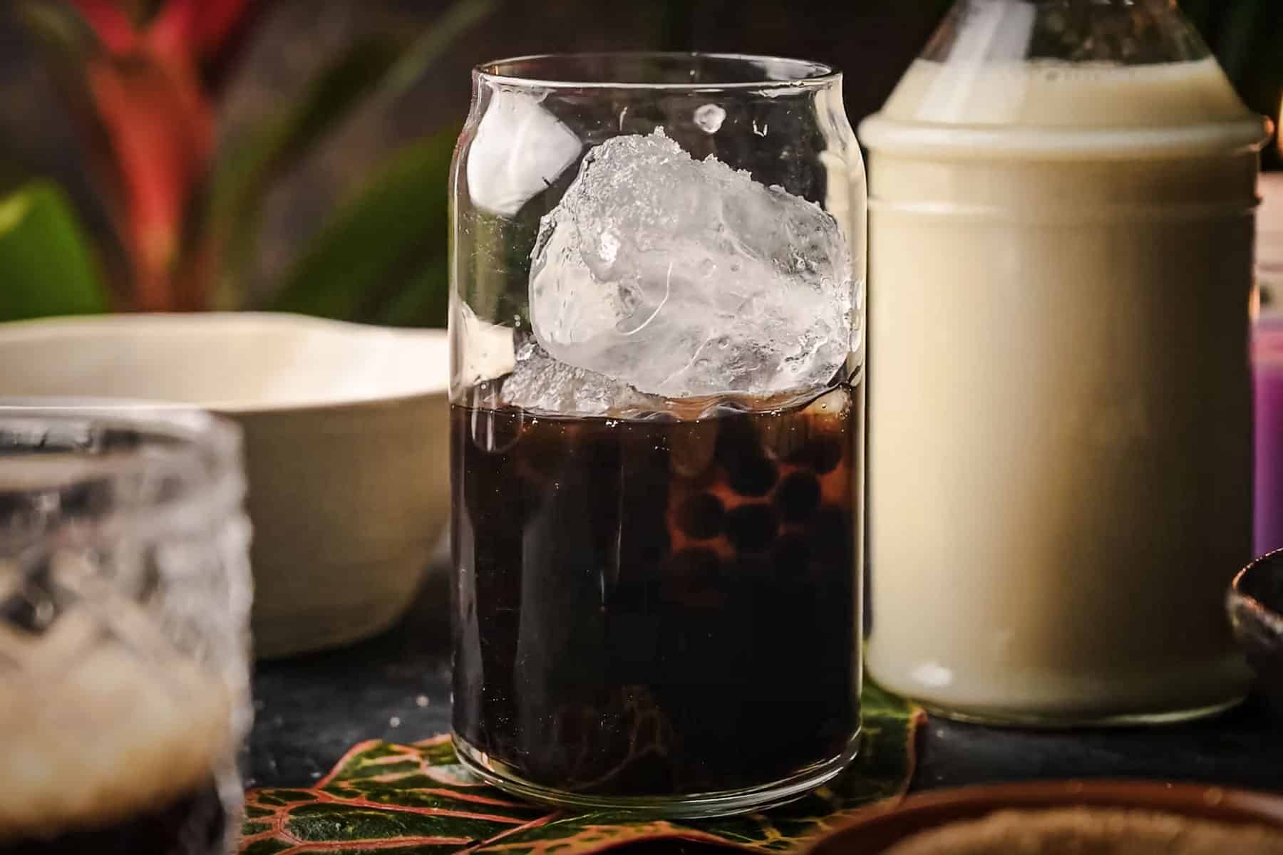 A glass of iced boba with large ice cubes sits on a dark table.