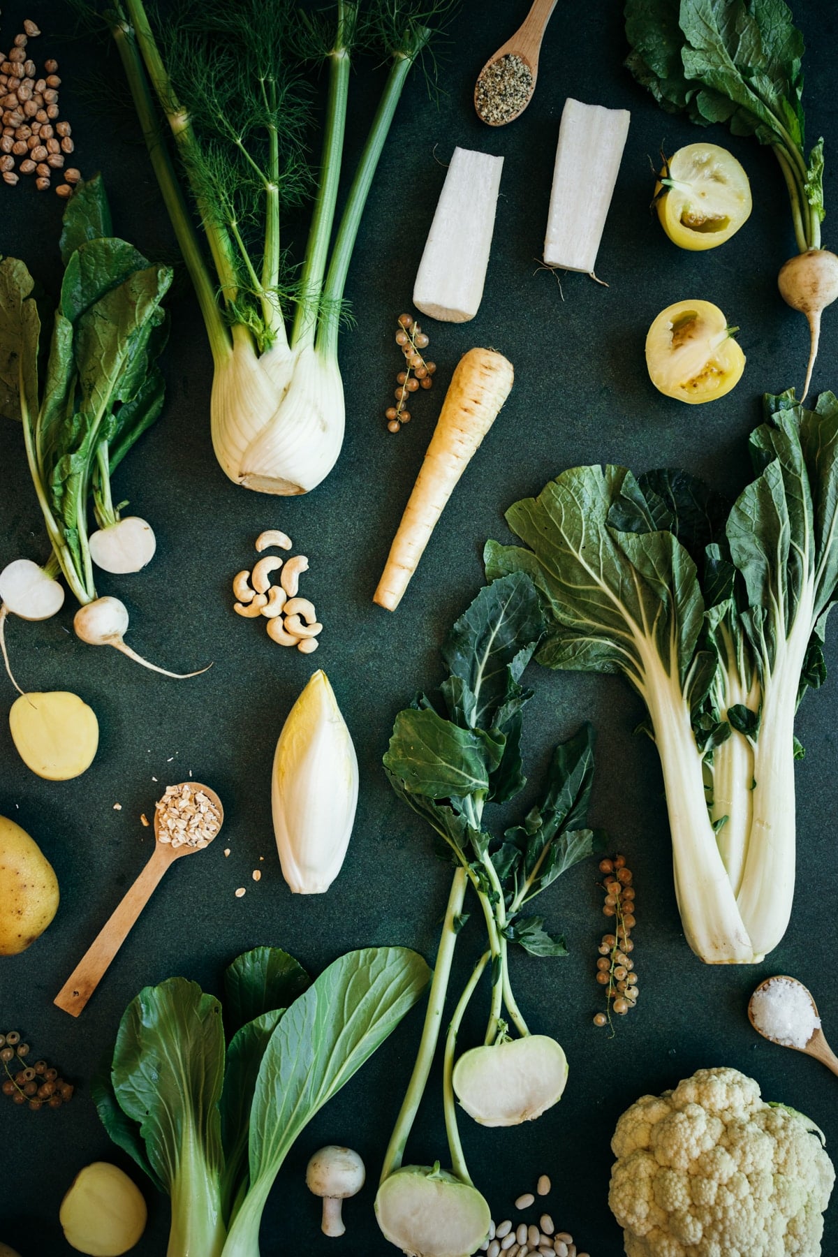 An array of white veggies and fruits on a green table.