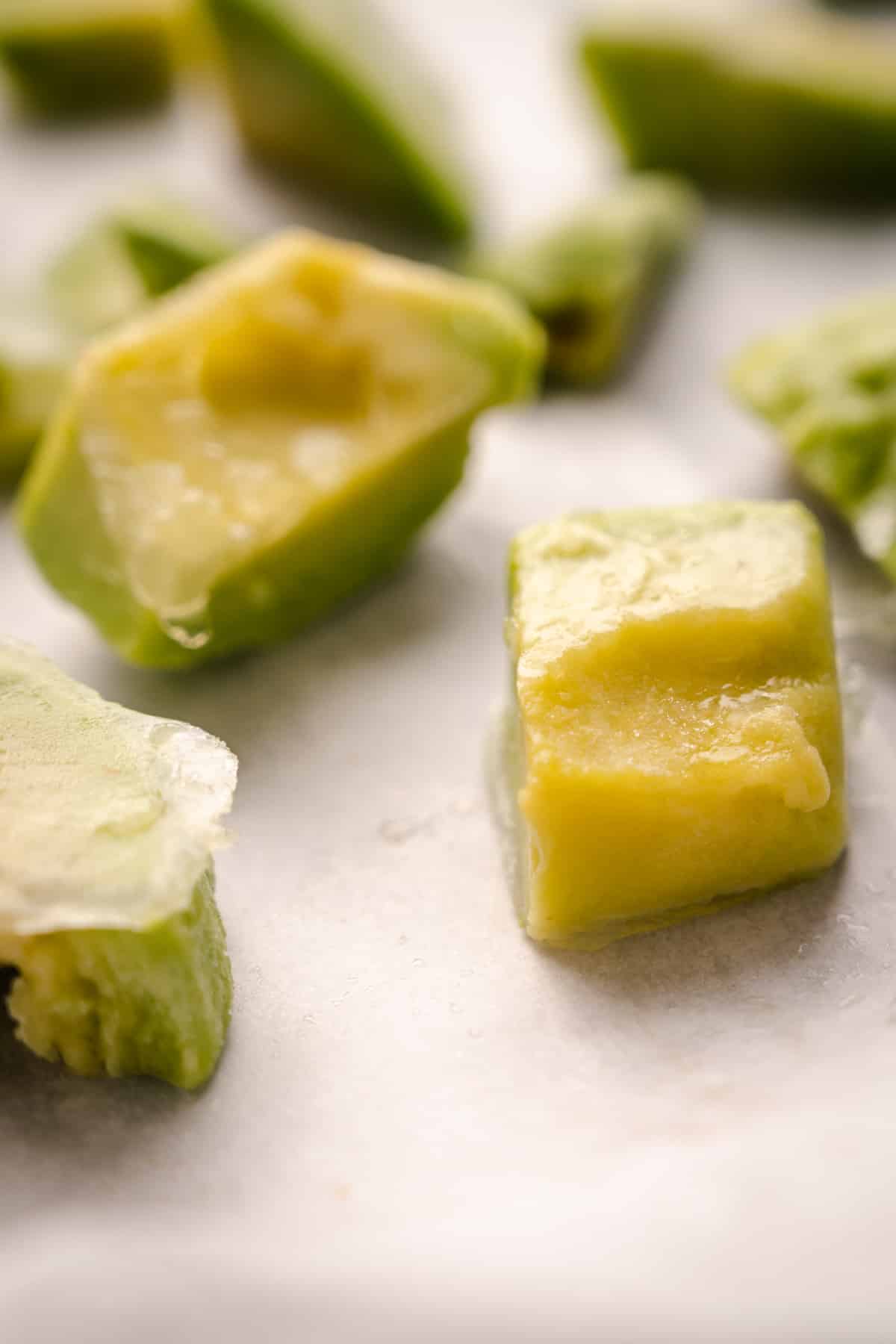 Frozen avocado chunks on a piece of white parchment paper.