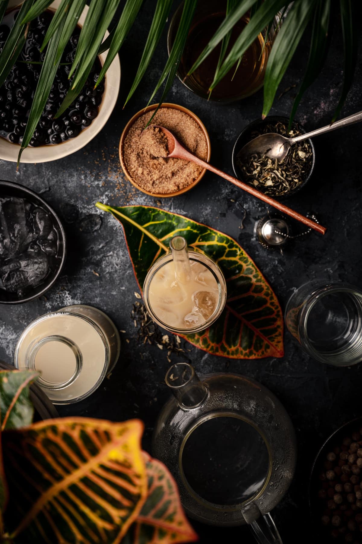 A variety of boba tea ingredients are arranged on a dark table.
