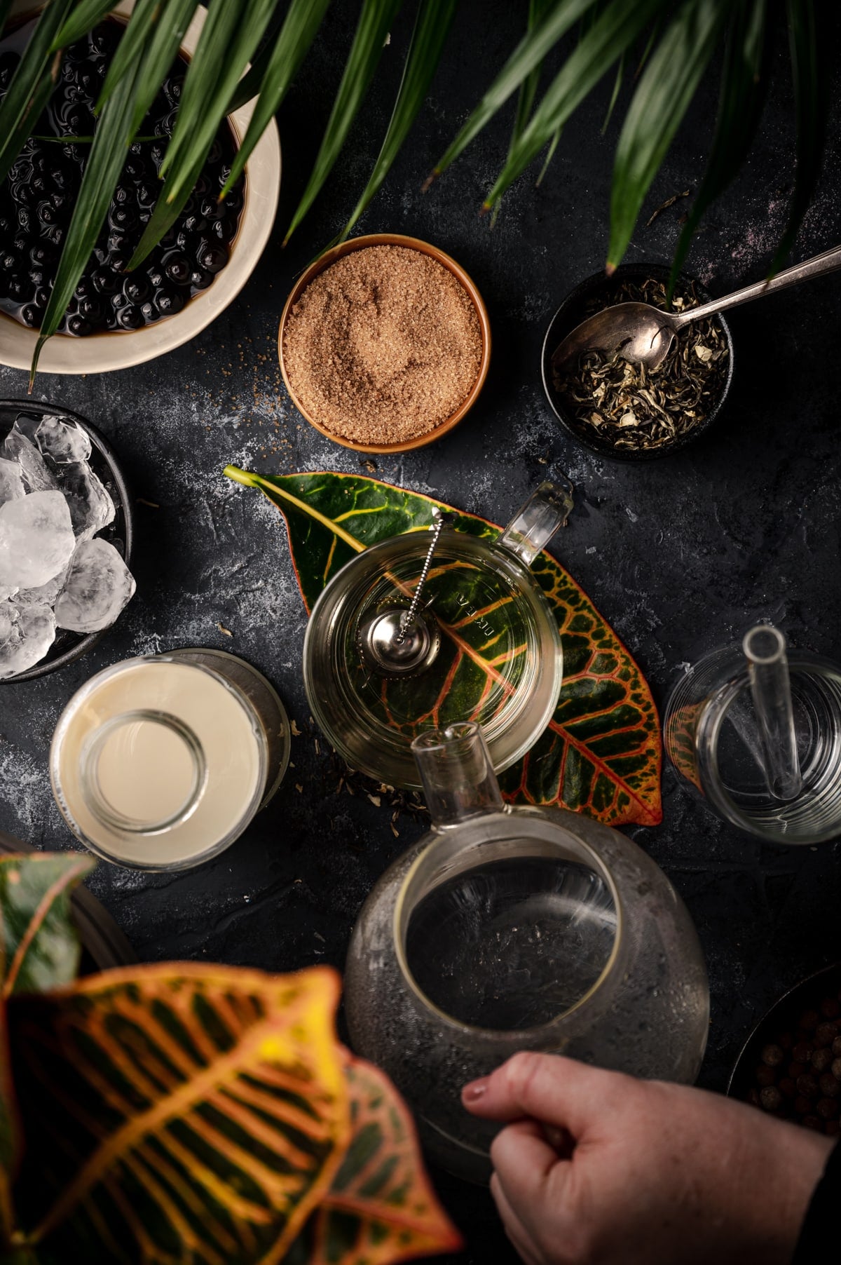 Metal tea infuser in a clear glass cup with hot water being poured over it.