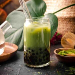 Matcha milk tea with boba in a clear glass with bubble tea straw.