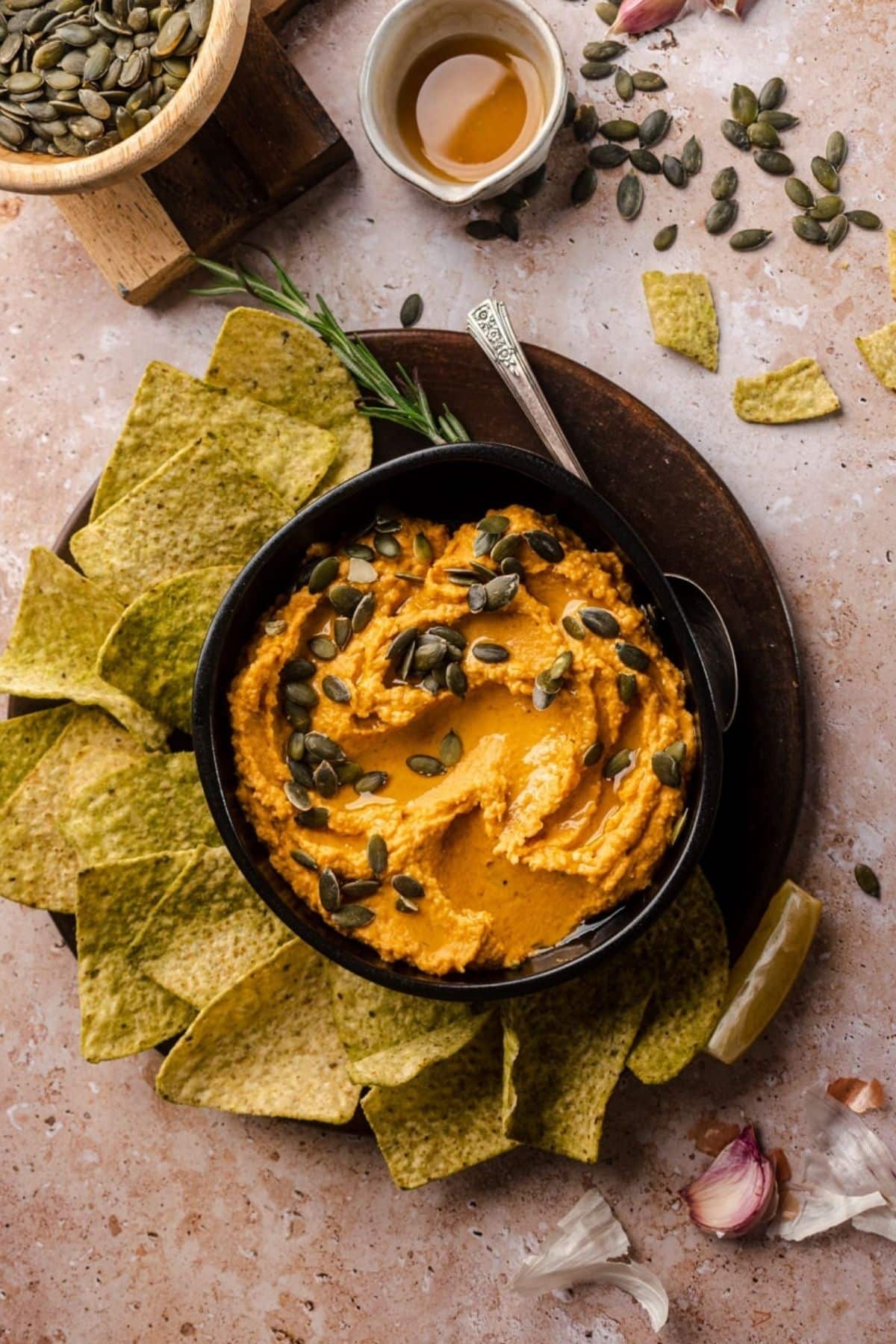 A bowl of pumpkin hummus topped with seeds, surrounded by green chips.