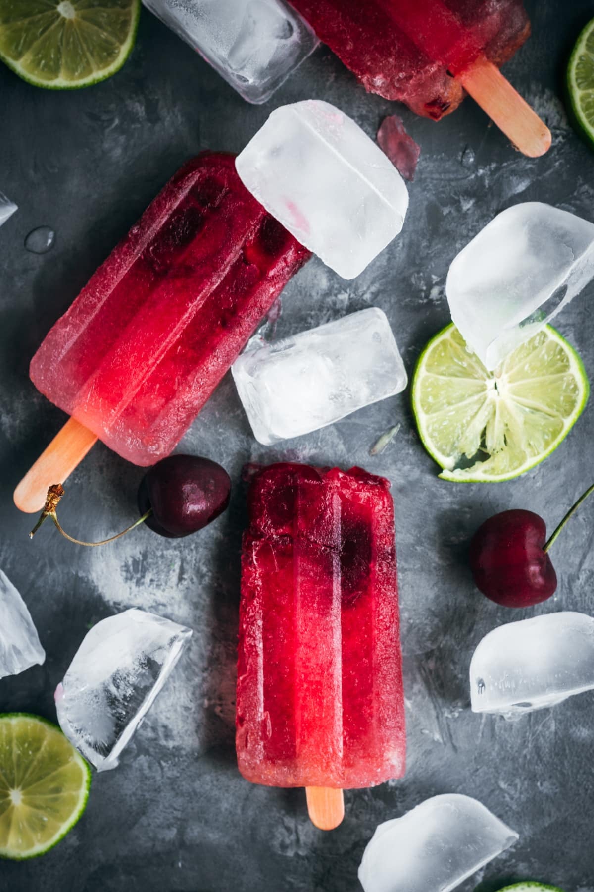 Cherry popsicles with ice cubes and lime slices.