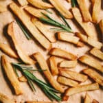 French fries on a baking sheet with rosemary sprigs.