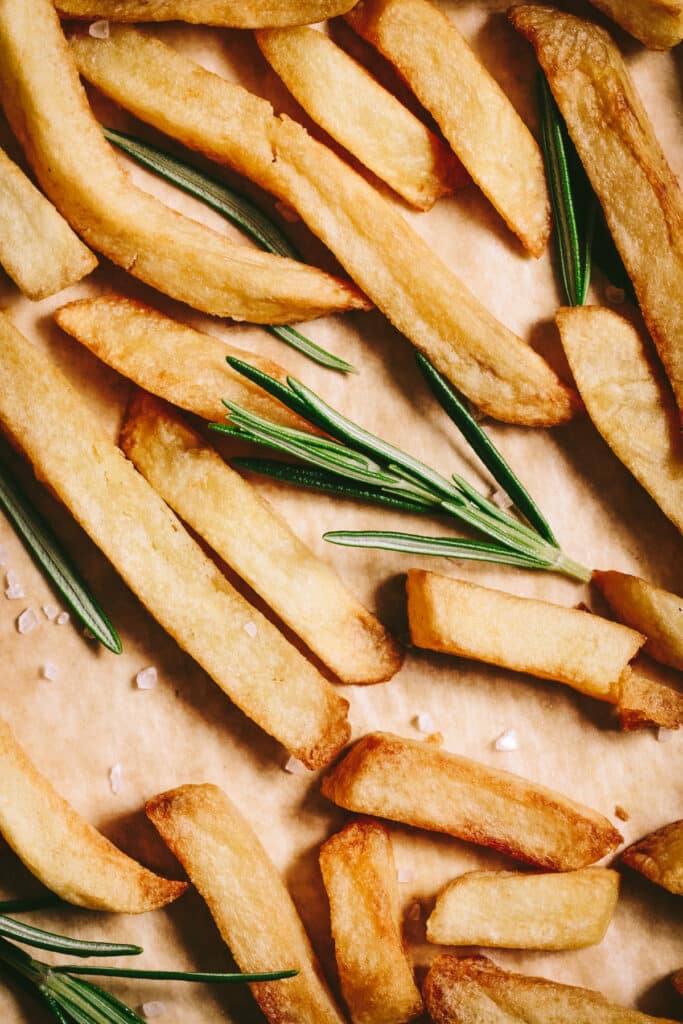 French fries with rosemary sprigs on a baking sheet.