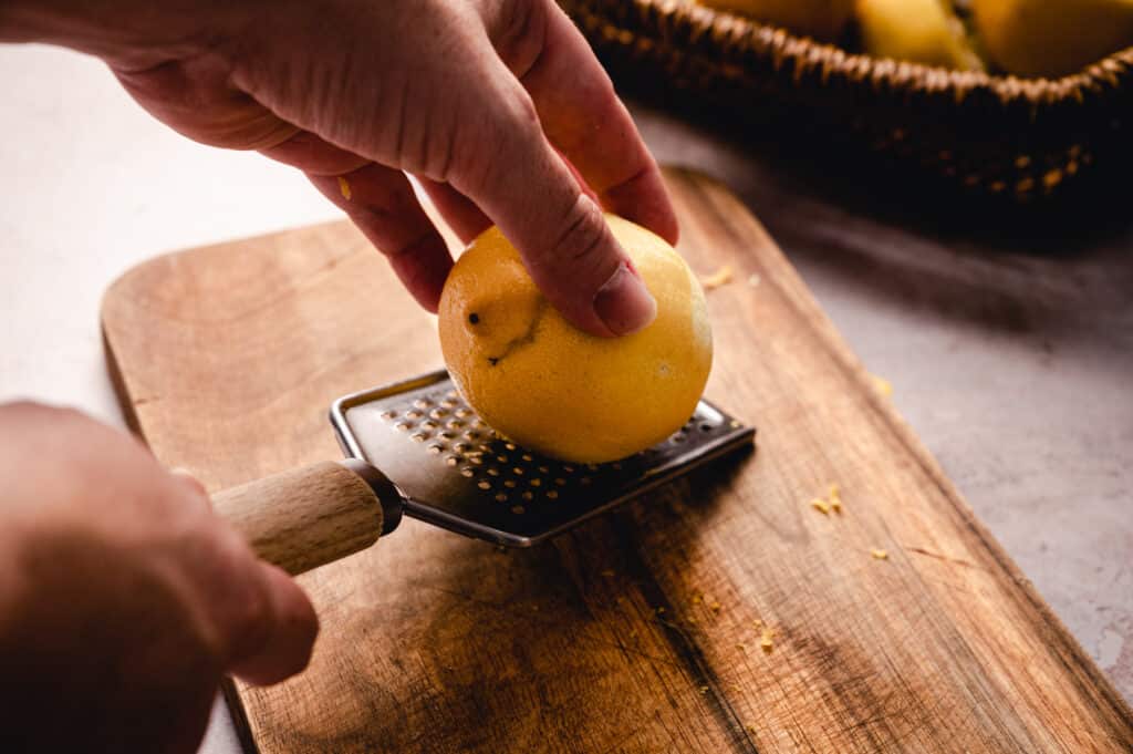 A person grating a lemon on a wooden cutting board.