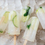 Five lime popsicles with fresh lime slices and mint leaves set on a bed of ice.