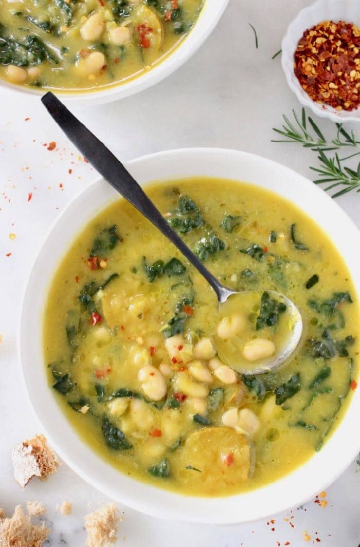 Two bowls of white bean and kale soup with a spoon.