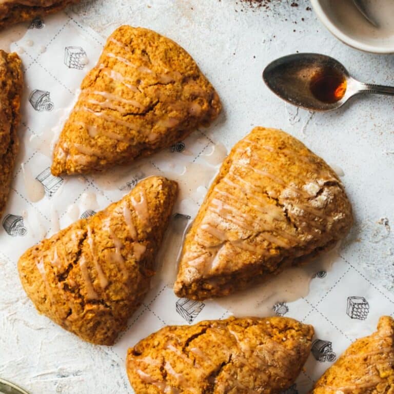 Five iced pumpkin scones are arranged on a patterned paper.