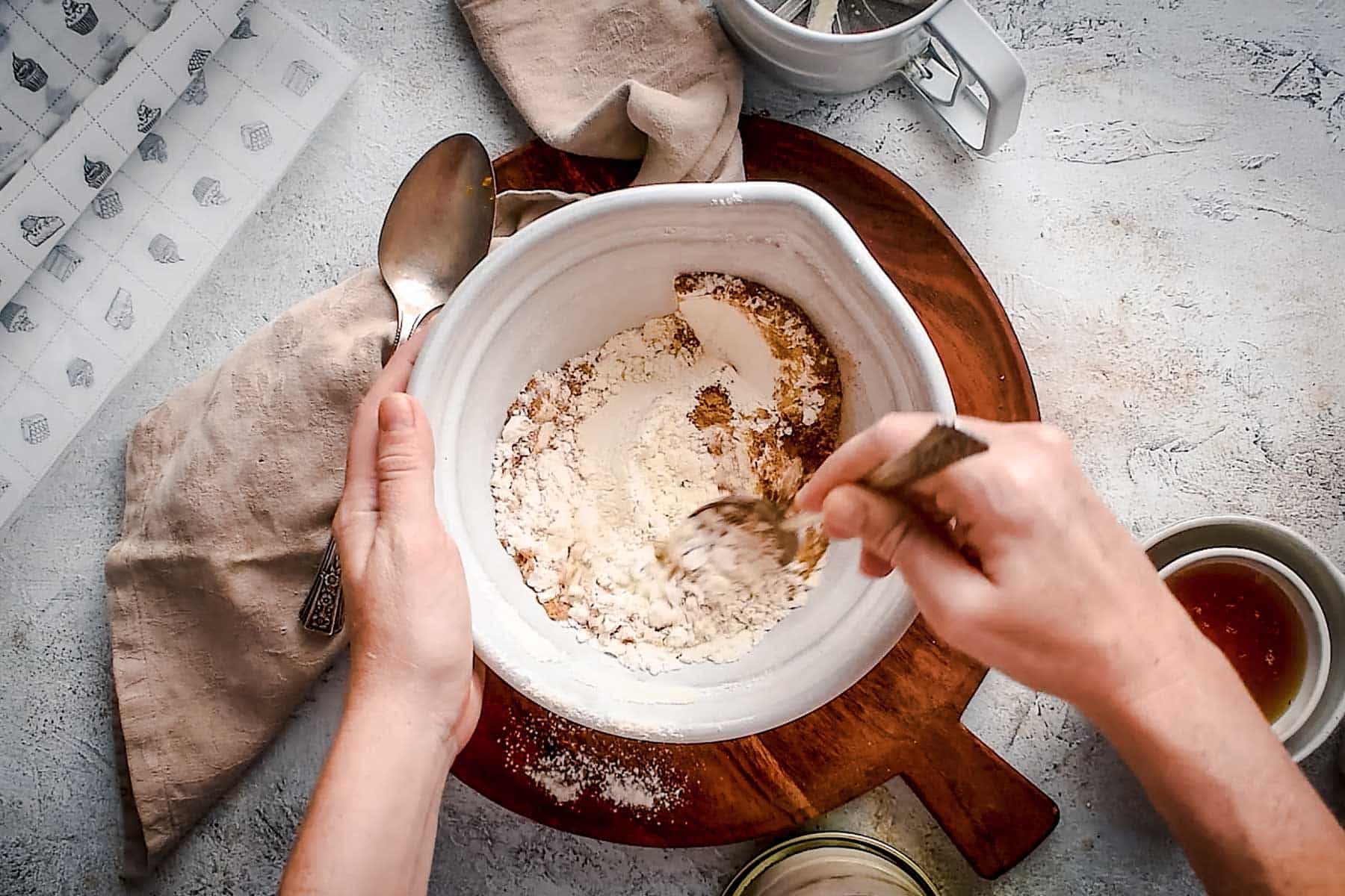 A person mixing flour and spices in a white bowl with a metal spoon.