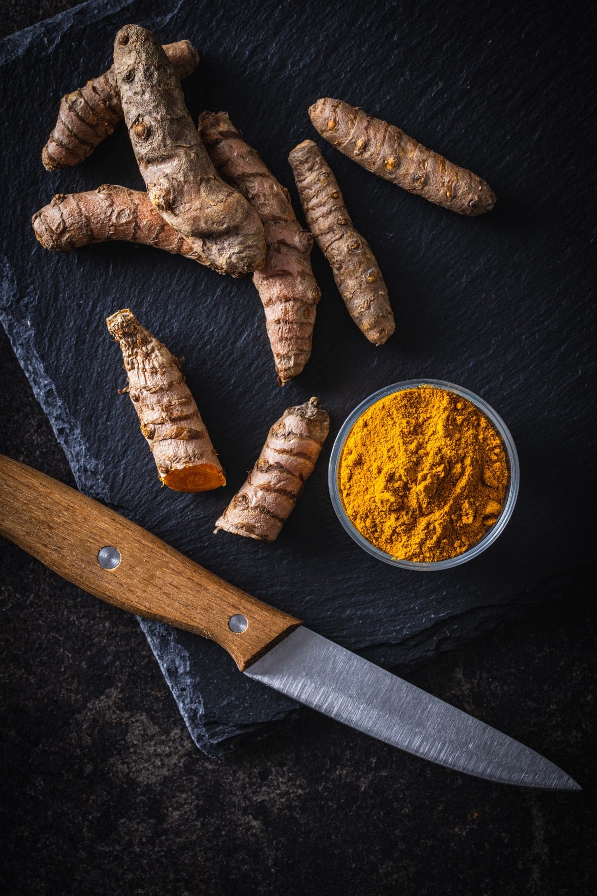Tumeric powder and a knife on a black background.