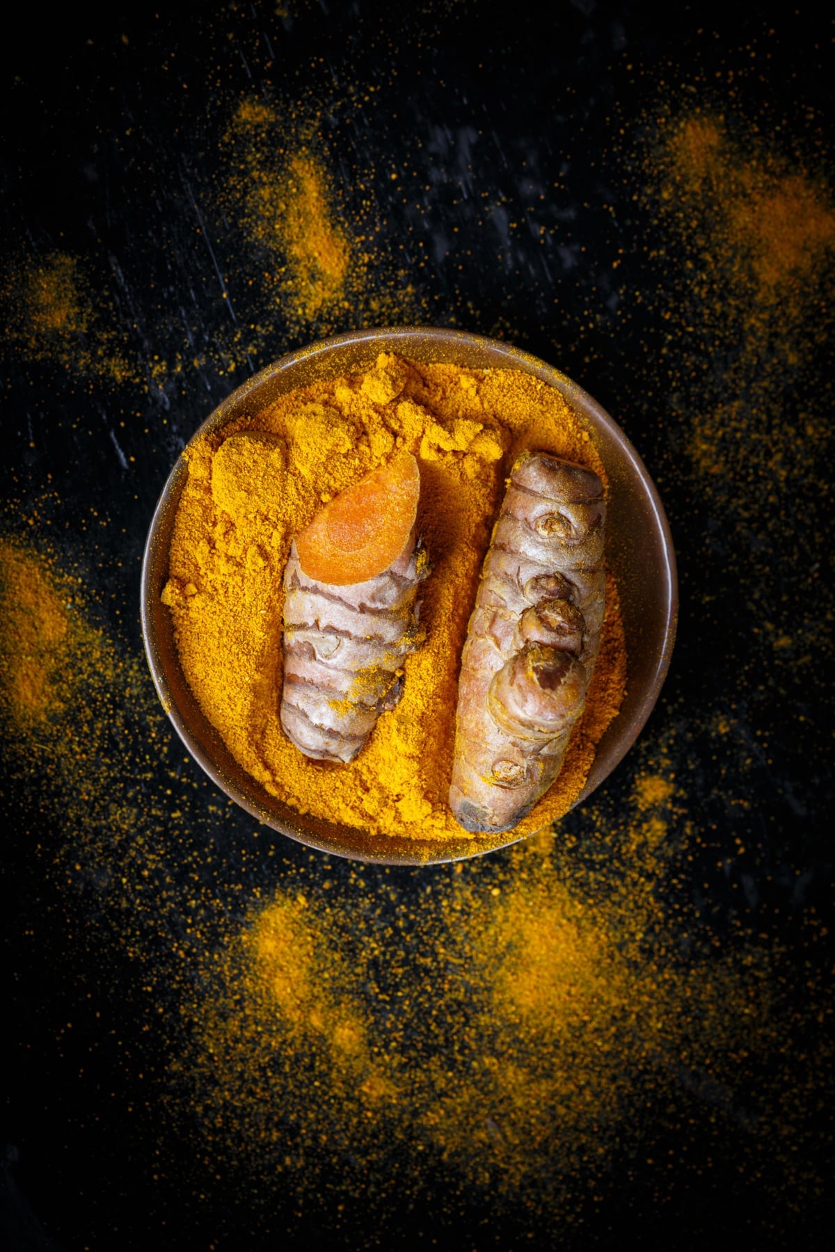 Tumeric powder in a bowl on a dark background.