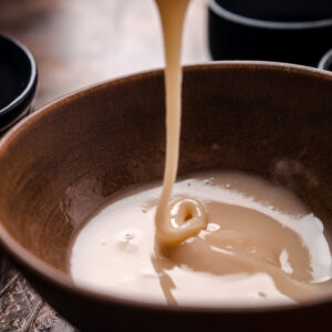 Pancake batter being poured into a brown bowl, creating a swirl of maple glaze in the center.