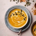 A bowl of creamy butternut squash soup topped with a swirl of coconut milk and pumpkin seeds.