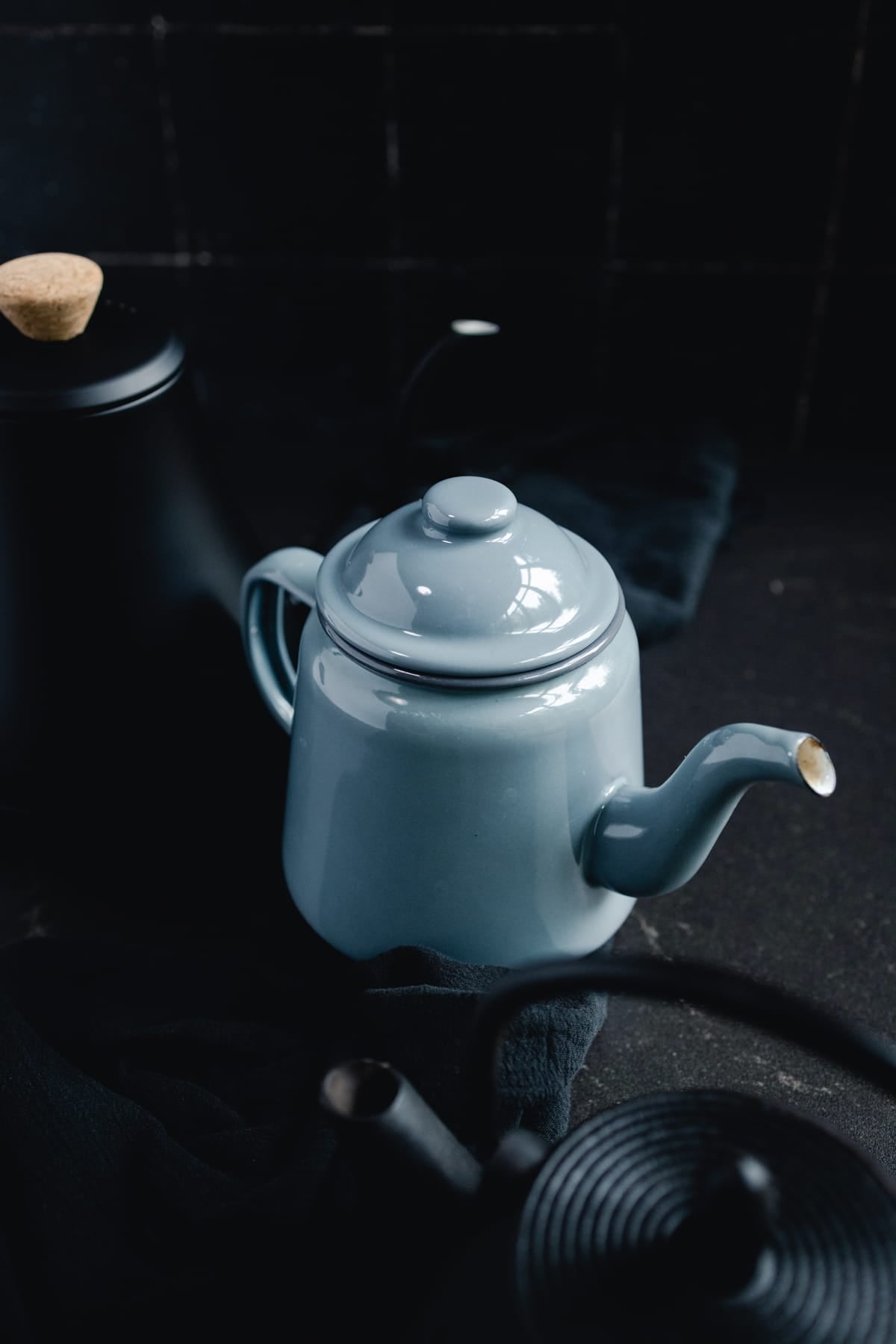 A blue-grey teapot and a black teapot on a table.