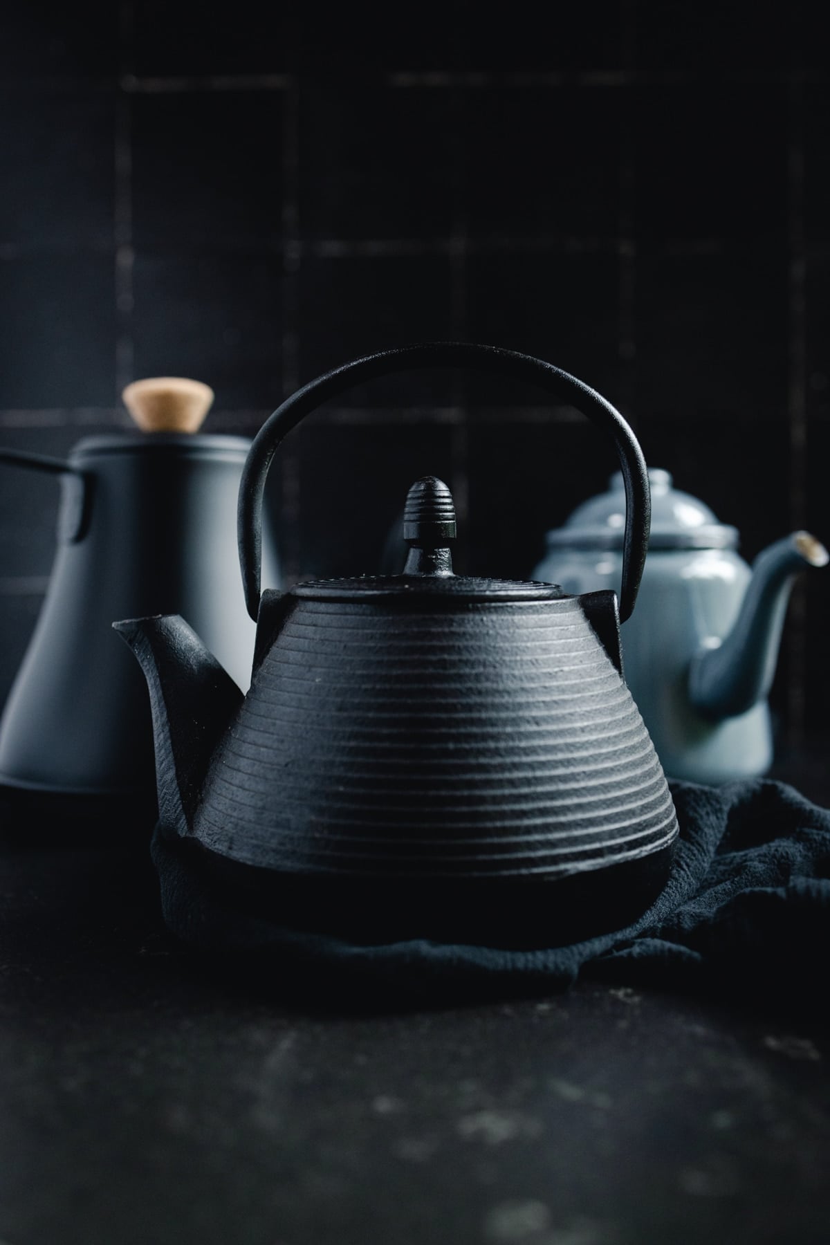 Two black teapots and a blue-gray one on a black background.