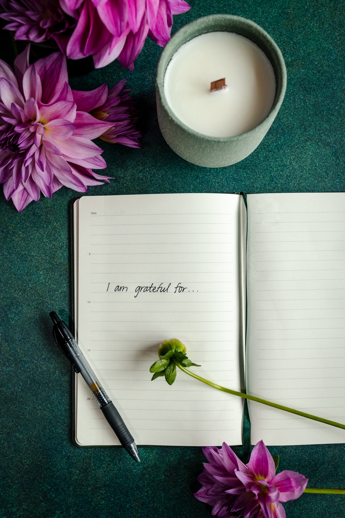 An open notebook with flowers and a candle on a green table.