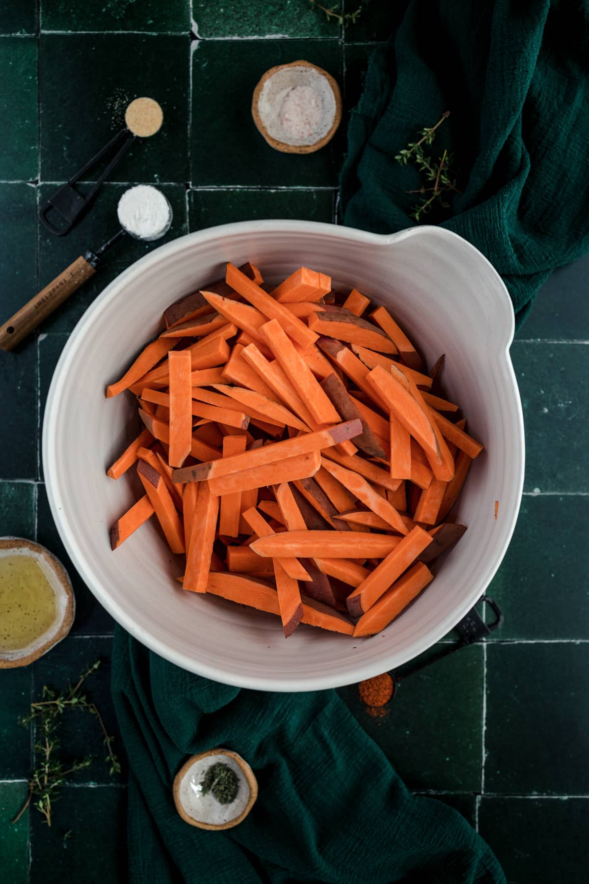 Sweet potato fries in a white bowl on a green tile.
