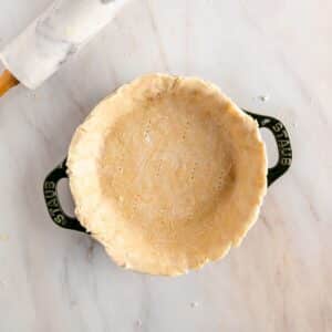 A vegan pie crust sits elegantly in a round baking dish on a marble surface, with the sheen of coconut oil shining subtly.
