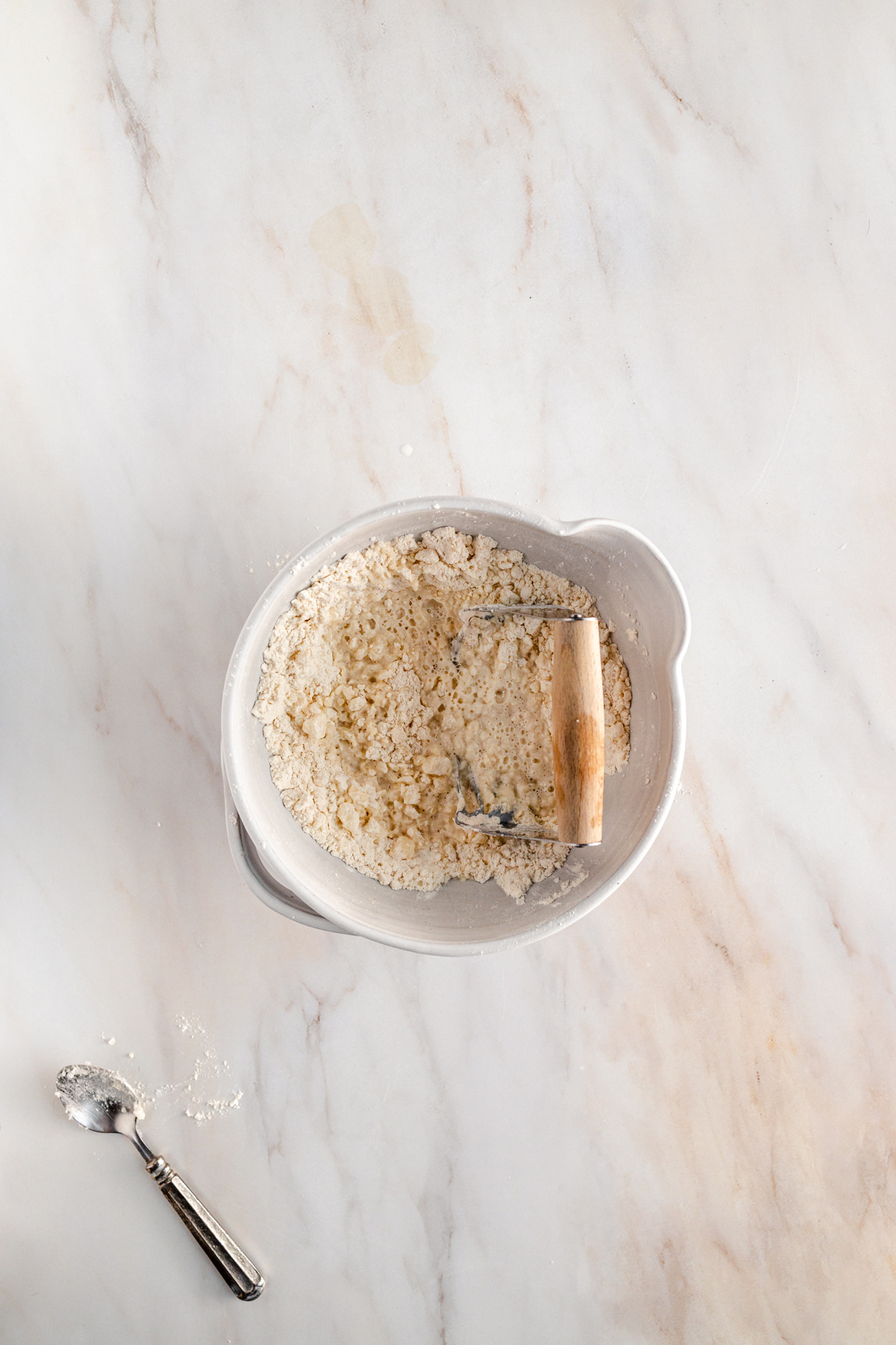 A bowl of flour and a measuring spoon on a marble table.