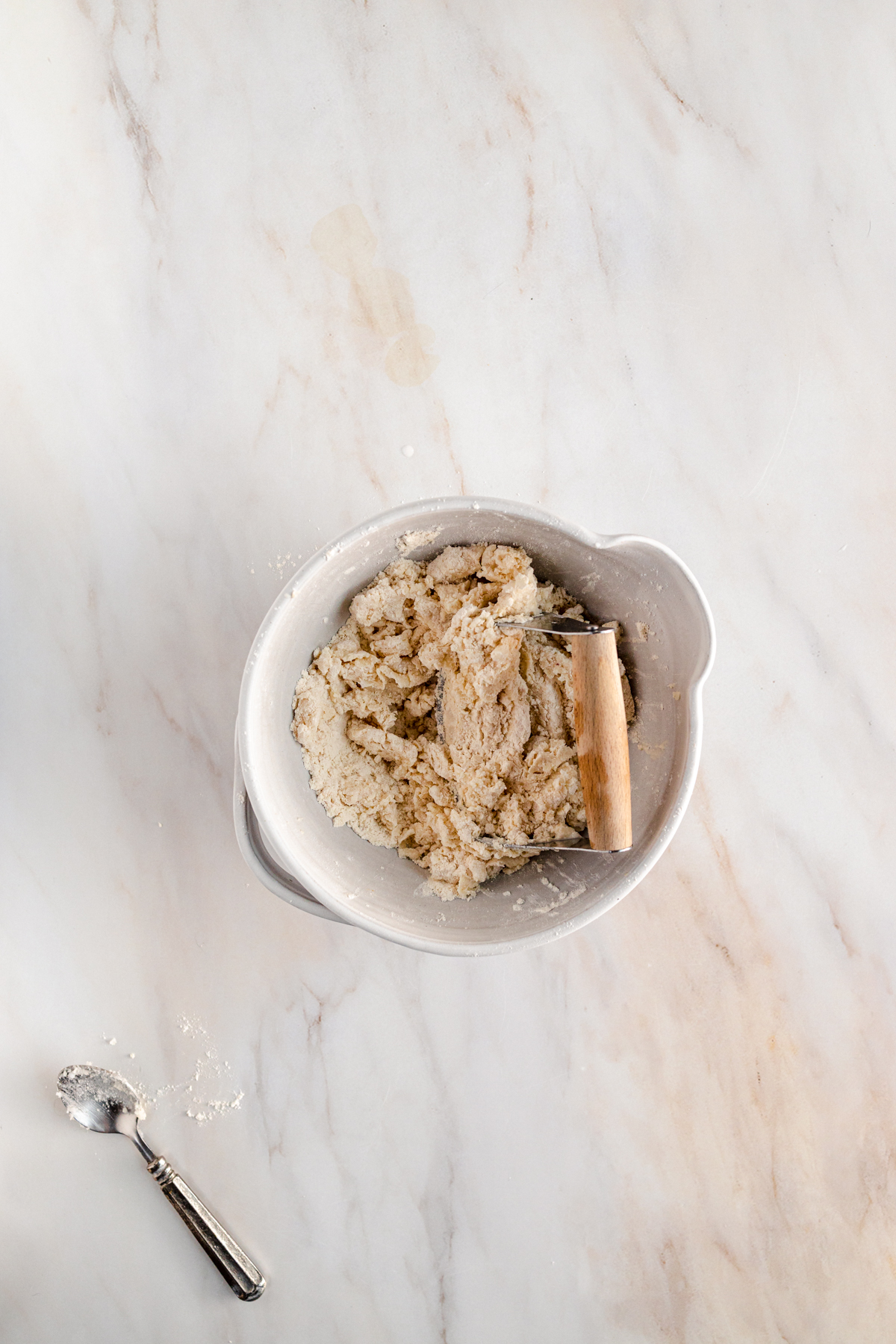 A bowl of flour and a spoon on a marble table.