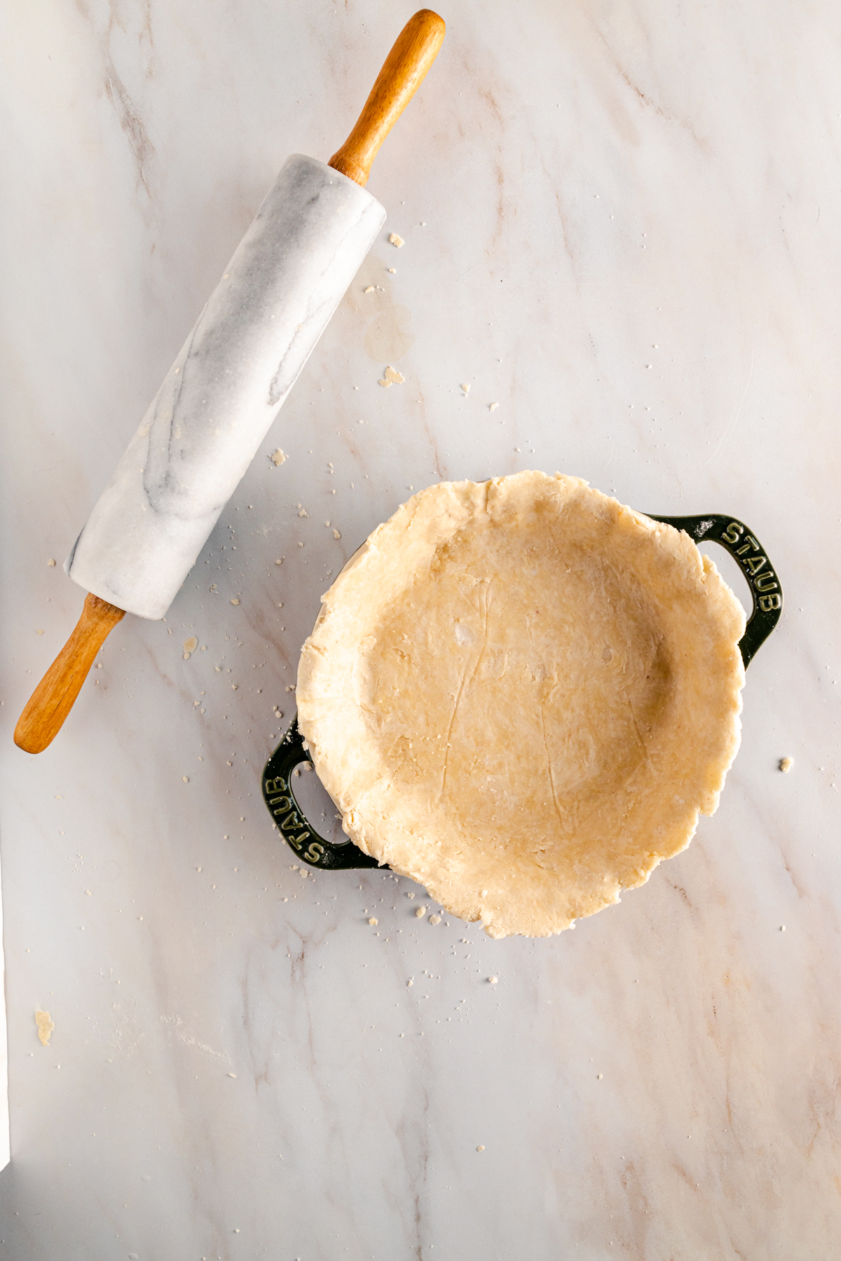 A pie crust and rolling pin on a marble countertop.