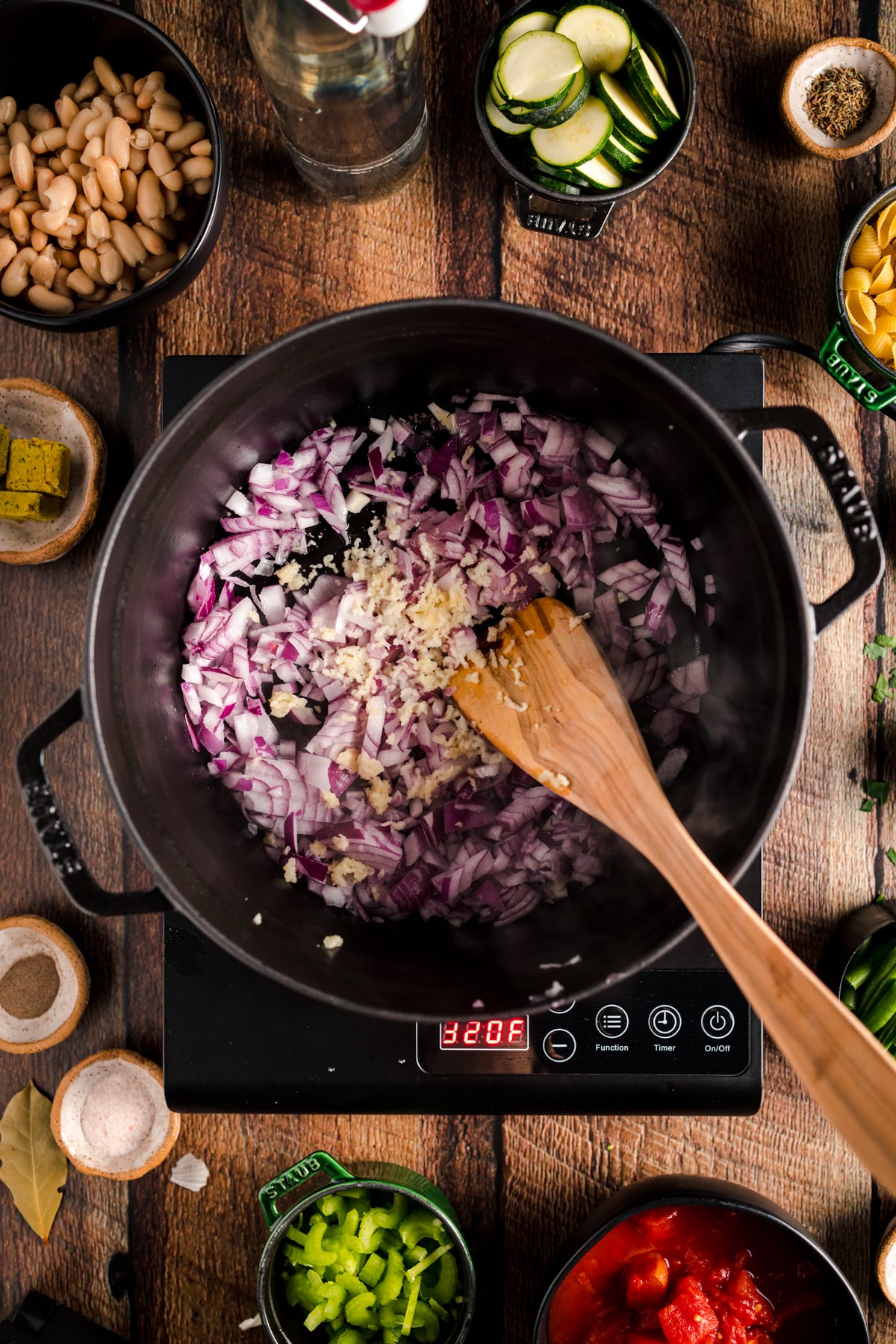 A pot with vegetables and a wooden spoon on a wooden table.