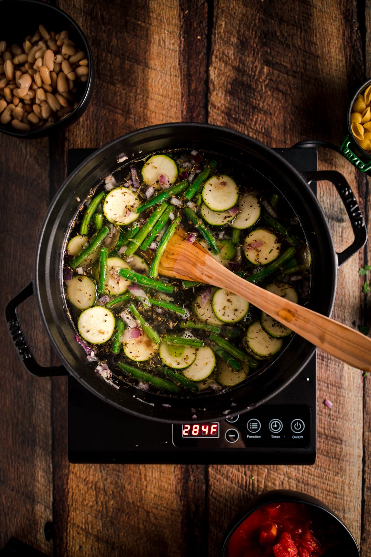 A pot with vegetables and a wooden spoon on a wooden table.