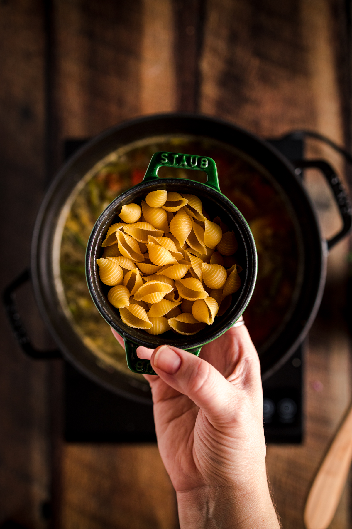 A person holding a bowl of pasta in front of a stove.