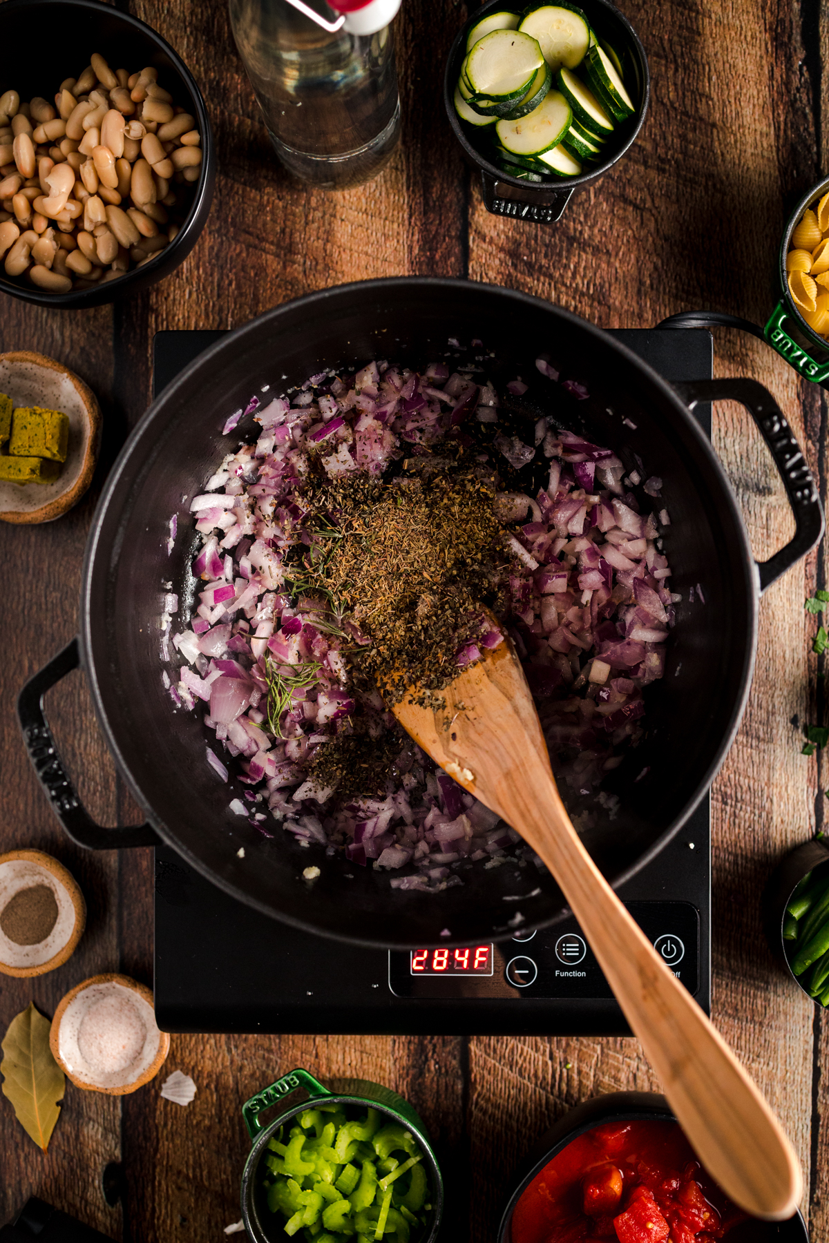 An electric skillet with vegetables and a wooden spoon.