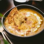 Bowl of creamy pumpkin curry soup topped with two slices of toasted bread and a swirl of coconut milk.