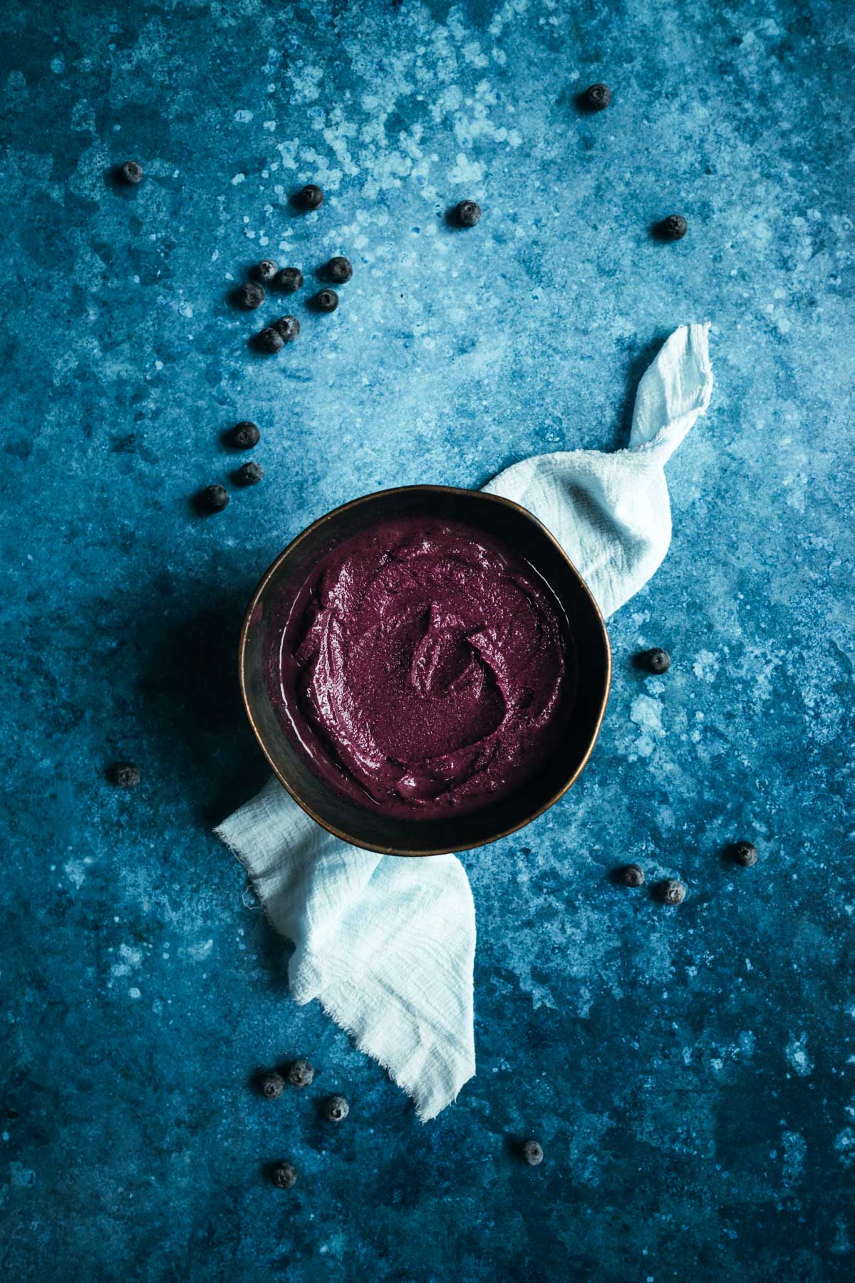 A bowl of acai blueberry smoothie on a blue background.