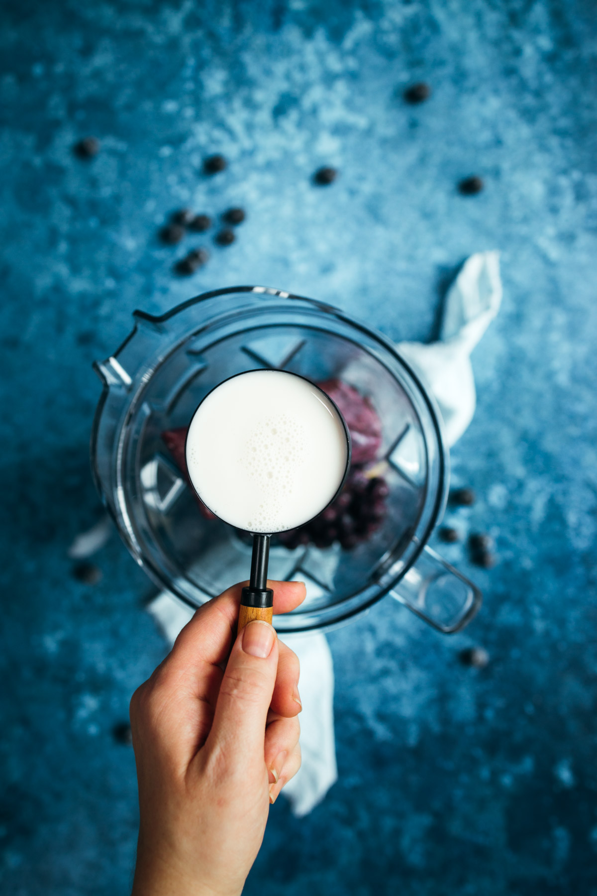 A hand holding a measuring cup of almond milk.