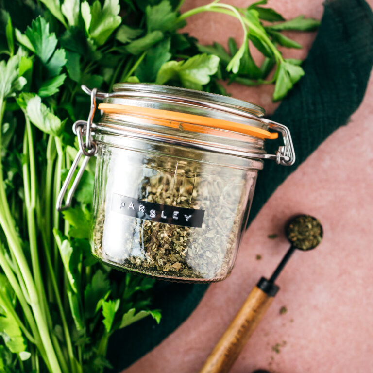 A glass jar with herbs on a pink background.