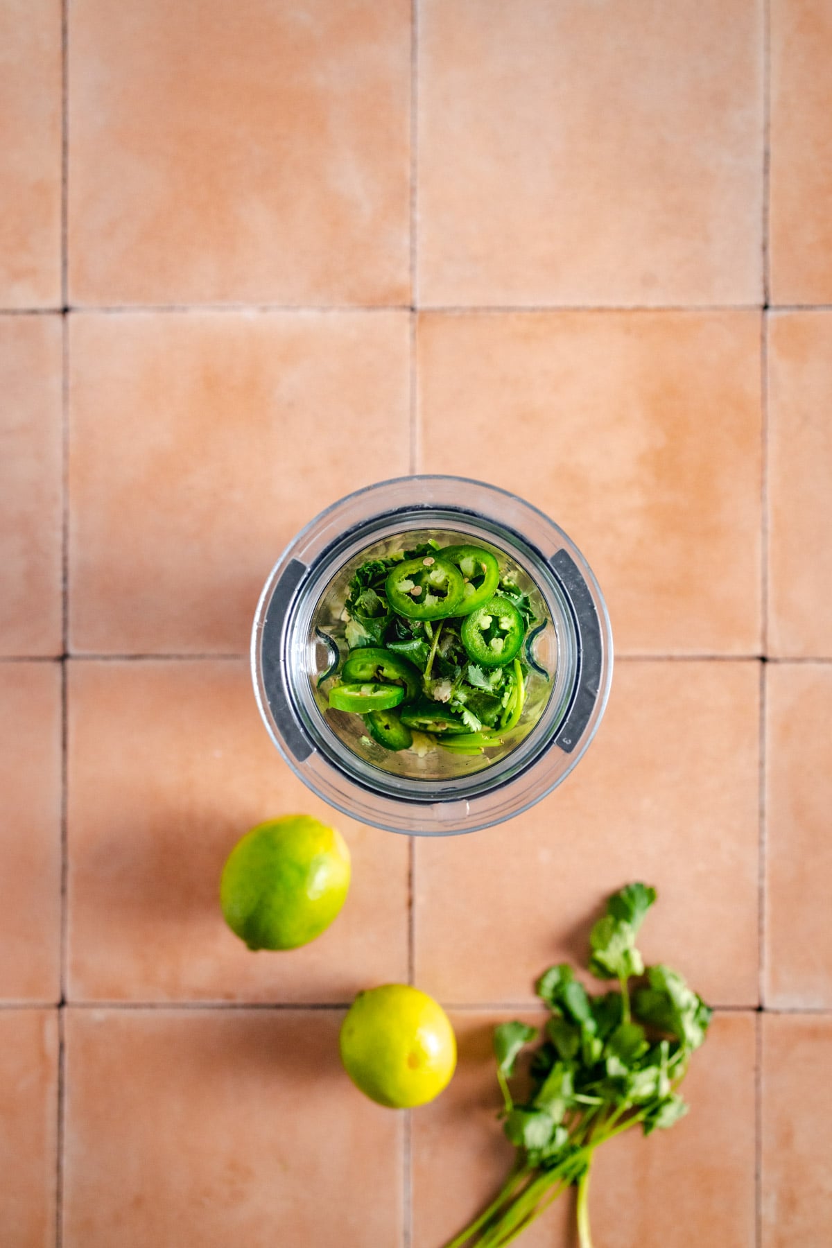 Jalapenos and limes in a blender on a tiled table.