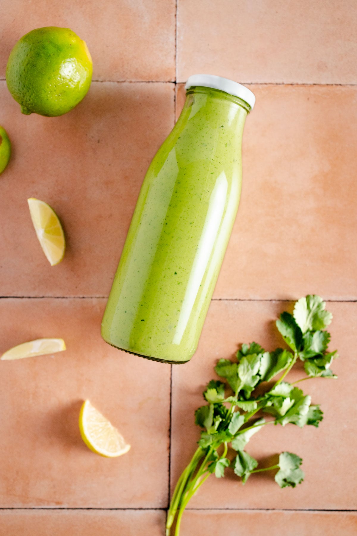 Glass bottle with white metal lid filled with green salad dressing.