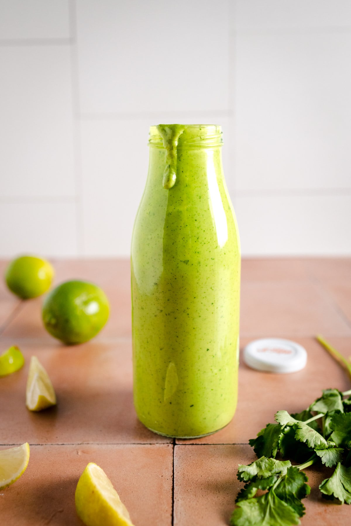 Cilantro lime dressing in a Le Parfait bottle with fresh lime and cilantro surrounding it.