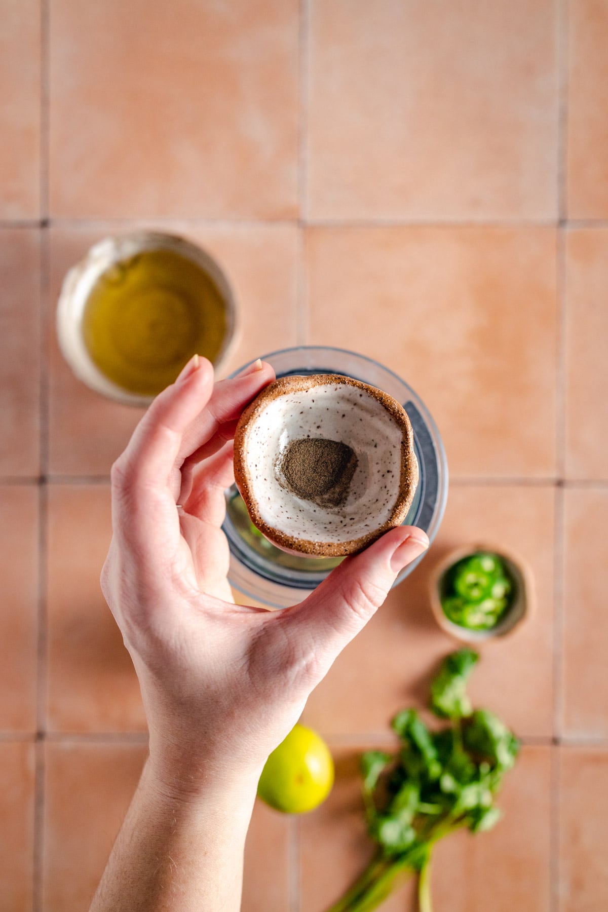 A hand holding a coconut in a bowl on a tiled floor.