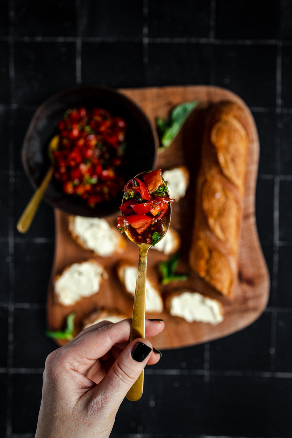 A person holding a spoon with tomatoes and bread.